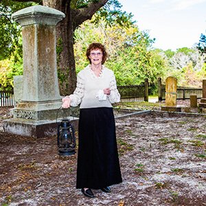 Costumed interpreter holding a lantern by a gravestone